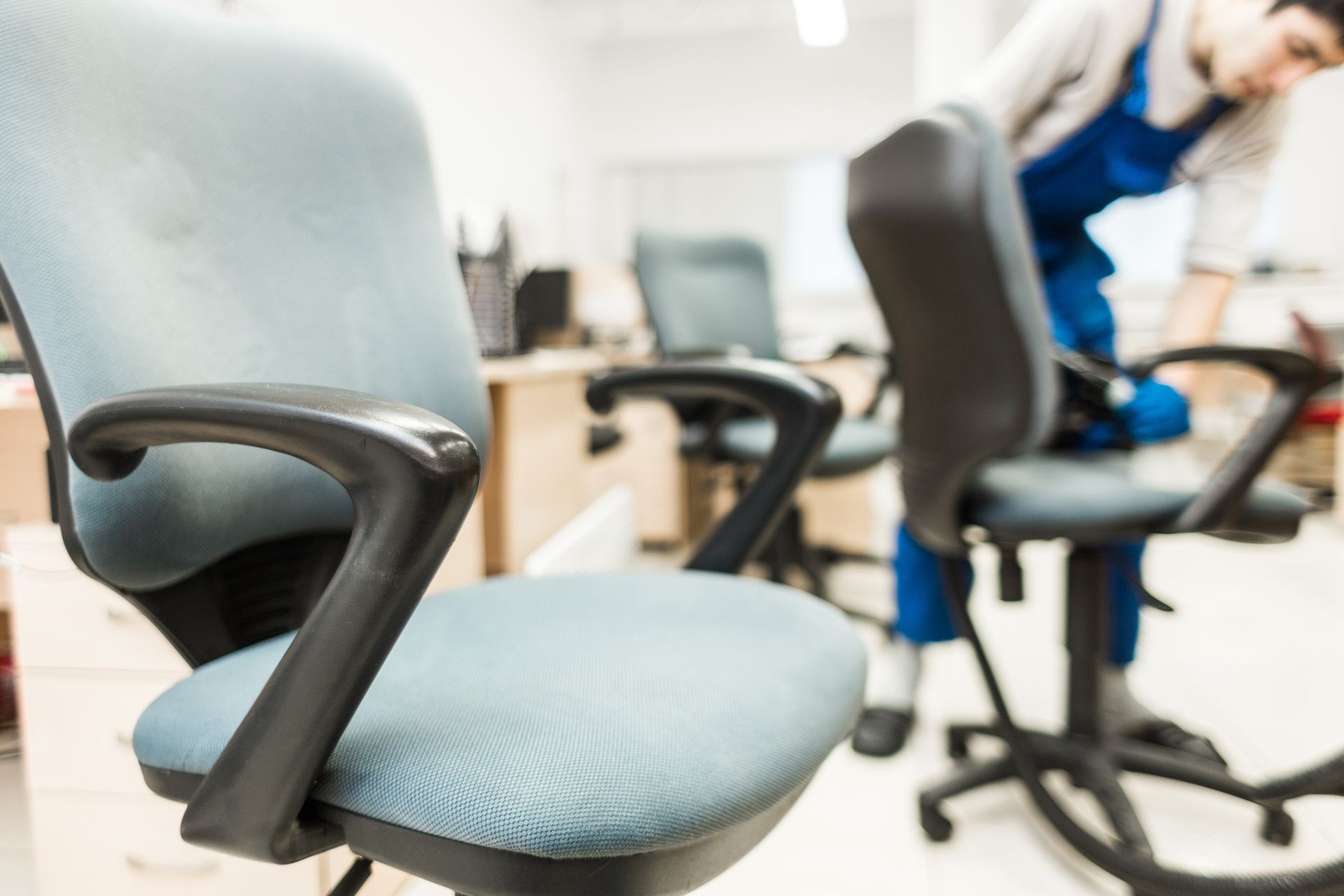 Young man in workwear and rubber gloves cleans the office chair with professional equipment.